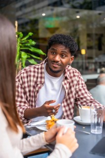 Young black man engaging in a lively conversation with a woman at an outdoor cafe table, enjoying