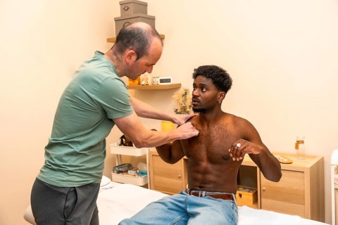 Physical therapist performing an examination and palpation on a young adult male patient's shoulder