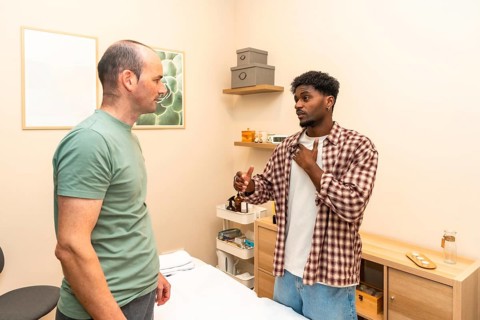 Two men in a counseling session engage in serious, supportive conversation in a clinical office,