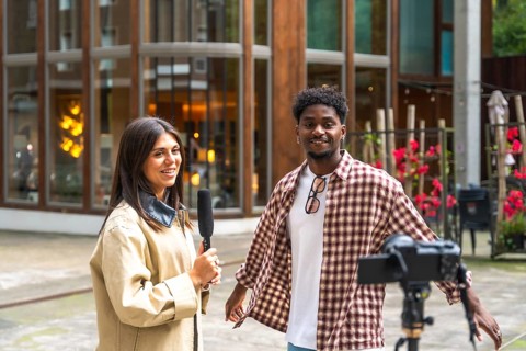 Journalist holding a microphone interviewing a young man on a city street, documenting the