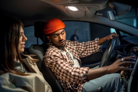 Young couple on a nighttime road trip, man driving while woman navigates and they chat over the