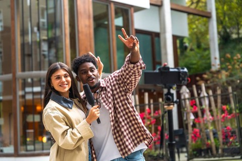 Diverse woman holding a microphone and smiling while man gestures cheerfully as they film a