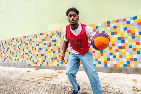 Young man actively playing street basketball, dribbling the ball with focus and energy against a