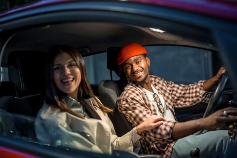 Smiling young diverse couple enjoying a pleasant car journey, with the man driving and the woman as