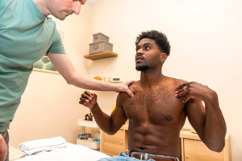 Male physiotherapist examining a young adult patient's shoulder and upper body, assessing mobility