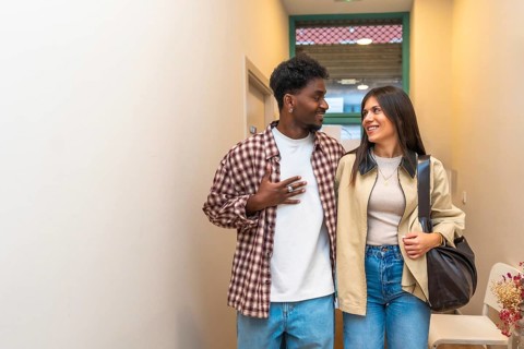 Young intercultural couple walking indoors, smiling and looking at each other with joy and