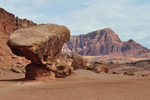 A gigantic rock sits on red desert sand in front of a barren rocky landscape, Grand Canyon National