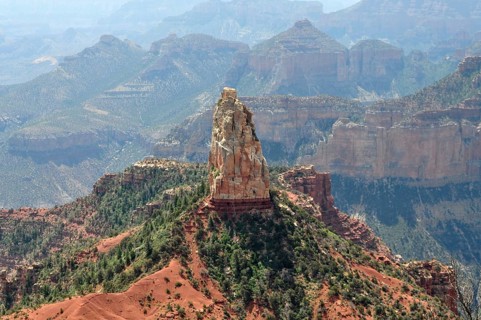 A distinctive rock formation rises in the midst of a rough and dry canyon landscape with wide