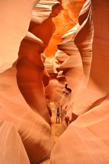 A traveler explores the narrow, winding passages of an orange slot canyon, Antelope Canyon, Navajo