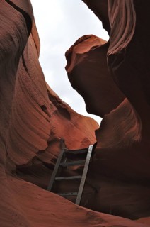 Steep sandstone rock walls with a ladder below and a view of the sky, entrance to Antelope Canyon,