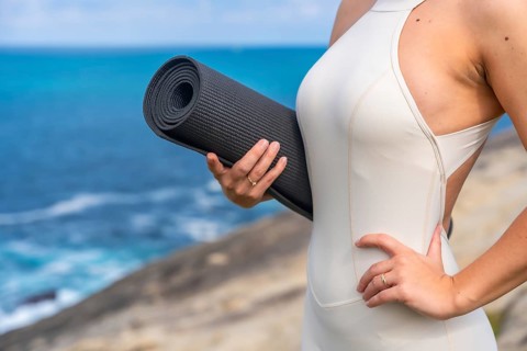 Woman standing outdoors holding a rolled yoga mat, preparing for a wellness and fitness session by