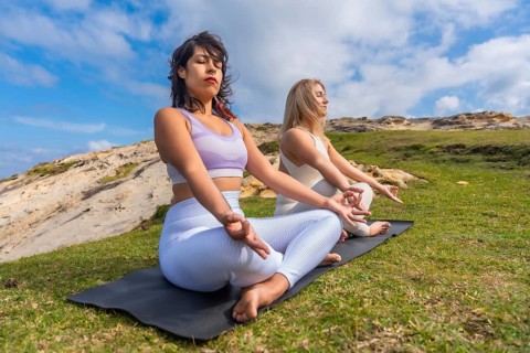 Two young women meditating on yoga mats outdoors, finding peace and mindfulness in nature,
