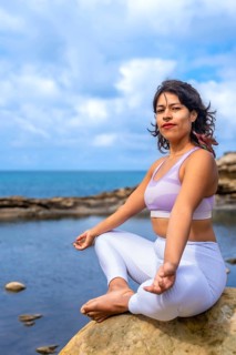 Woman sitting in a lotus position on a rock by the ocean, practicing yoga and finding inner peace,