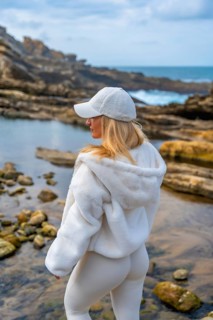 Woman in comfortable hoodie and leggings meditating on rocky coast, back to camera, finding calm