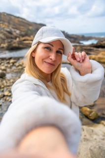 Happy woman smiling to camera and adjusting her white cap, enjoying a casual outdoor moment on a