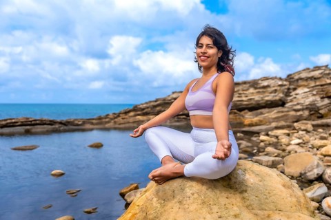 Woman practicing lotus yoga on a coastal rock, meditating peacefully at the sea's edge, embracing