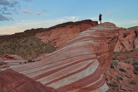 Person standing boldly on a striped cliff in the middle of the desert, Valley of Fire State Park,