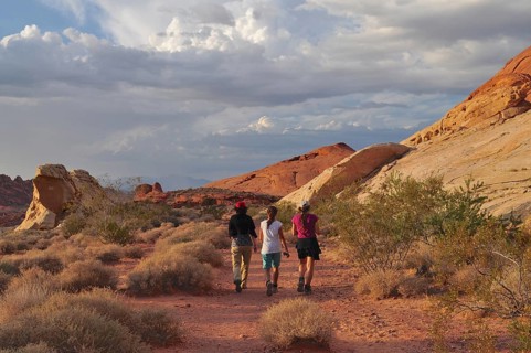 Three hikers on a trail through a desert landscape with clouds, Valley of Fire State Park, Nevada,