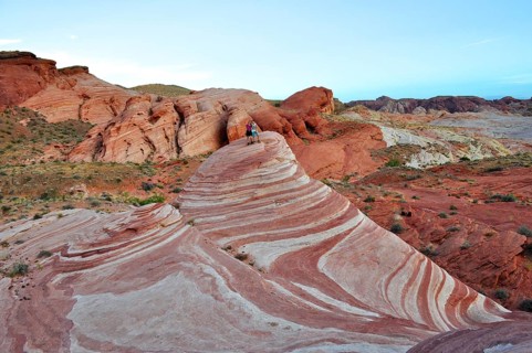 Two people standing on a striped rock formation in a desert landscape, Valley of Fire State Park,