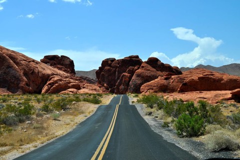 Lonely road leads through red rocky landscape in the desert under blue sky with clouds, Valley of