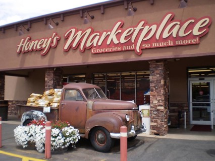 Old Studebaker pickup truck full of flowers parked in front of a nostalgic market building, Honey's