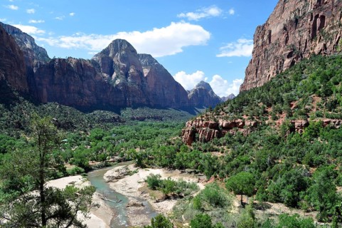 River flows through a lush valley surrounded by imposing mountains and green vegetation, Zion