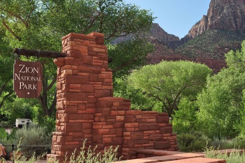 Brick monument with sign in Zion National Park, surrounded by green trees and mountains, Zion