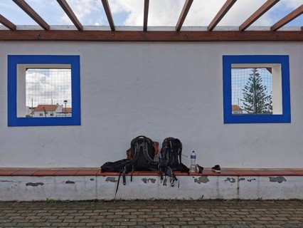 Two backpacks on a bench in front of a white wall with blue window cutouts, hiking on the