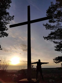 A large cross and a silhouette of a person at sunset, view over Kronach from Kreuzberg, Frankenwald