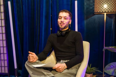 Young man wearing headphones around his neck and holding papers. Actively engaging. Communicating.