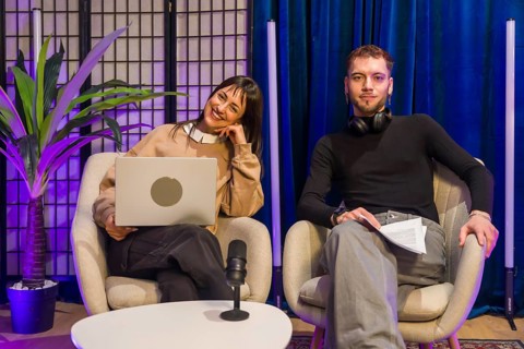 Two young content creators, a smiling woman with a laptop and a man with headphones, sitting on