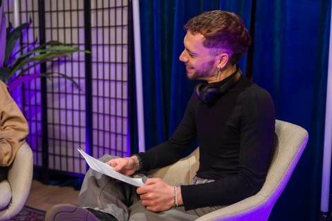 Man in a modern studio setting holding notes and smiling while recording a podcast or creating