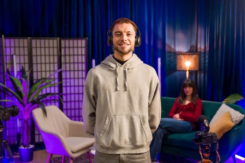 Content creator standing and smiling, wearing headphones in a modern recording studio setup with a
