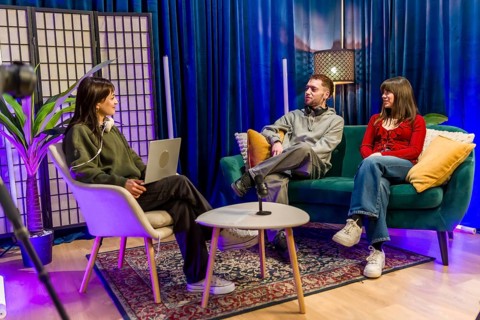 Young men and women are collaborating and talking in a colorful studio setting, recording a podcast