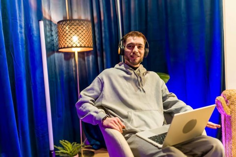 Young man wearing headphones and hoodie, sitting comfortably with a laptop in a home studio,