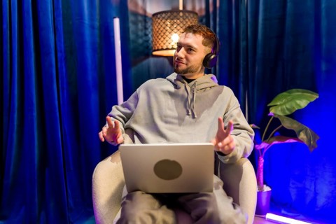 Young man wearing headphones and using laptop, recording a podcast or live streaming content from
