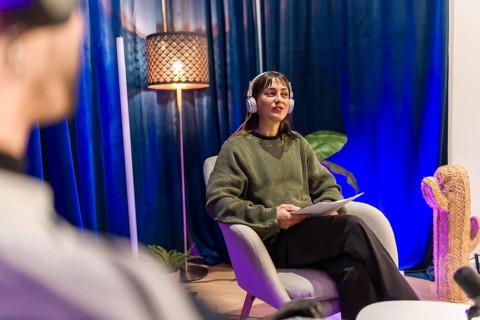 Young woman wearing headphones and holding notes, speaking into a microphone while recording a