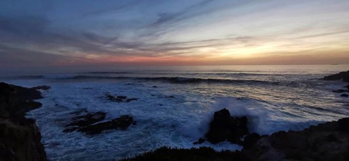 Dramatic sunset with dark clouds and waves, rocks in the foreground, hiking on the Fisherman's