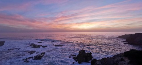 Romantic sunset over the sea with pink sky and dark rocks, hiking on the Fisherman's Trail,