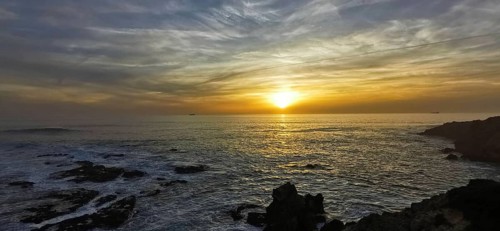 The picture shows an atmospheric sunset over the sea with dramatic clouds, hiking on the
