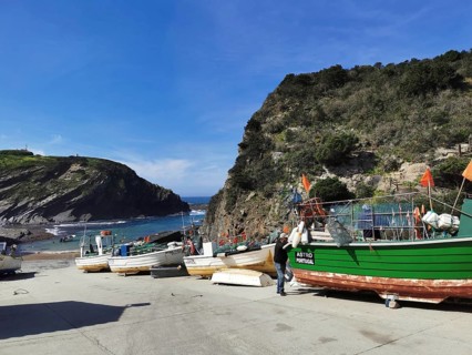 Small harbor with colorful fishing boats against a rocky coastal backdrop, hiking on the