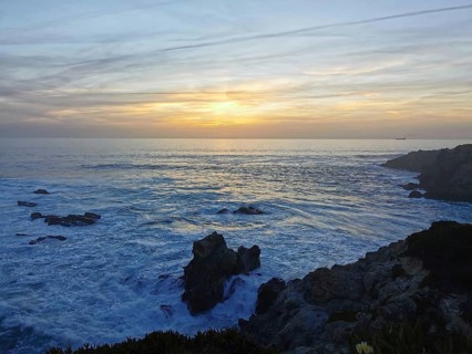 The sunset draws bright colors across the sea as waves hit the rocks, hiking the Fisherman's Trail,
