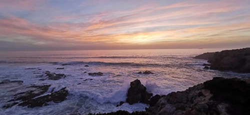 A gentle sunset with pastel-colored sky over the roaring sea, hiking the Fisherman's Trail,