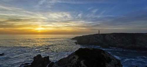 A coastal scene with a lighthouse at sunset. The clouds color the sky colorful, hiking on the