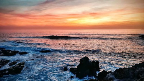 Impressive sunset with orange sky and dark rocks by the sea, hiking on the Fisherman's Trail,