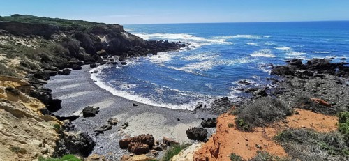 A rocky stretch of coast with a view of the blue sky and the rushing sea, hiking on the Fisherman's