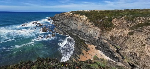 Coastal landscape with eroded rock formations and breaking waves on a sandy beach, hiking on the