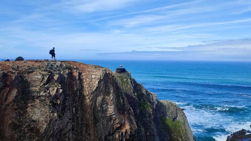 Lone hiker on rocky cliff overlooking the vast ocean, stork's nest (ciconia), Fisherman's trail,