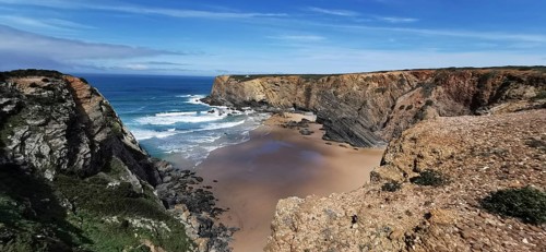 Wide sandy bay surrounded by rugged cliffs with gentle waves, hiking on the Fisherman's Trail,
