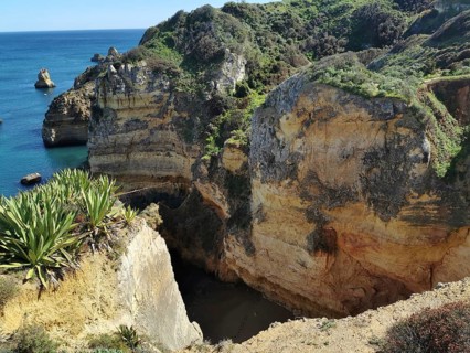Steep coastal cliffs with green vegetation and deep blue sea in the background, Lagos, Algarve,